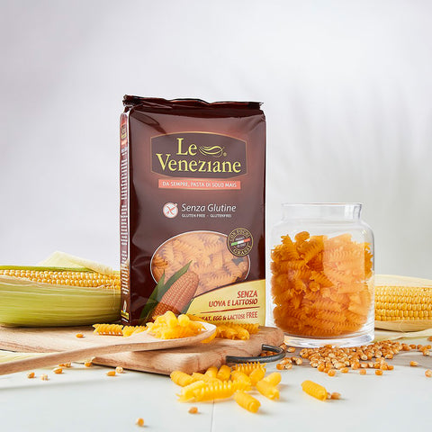 One packet of Le Veneziane Gluten Free Pasta Eliche Spirals, pictured with corn in background and loose pasta spirals on benchtop surrounding box.